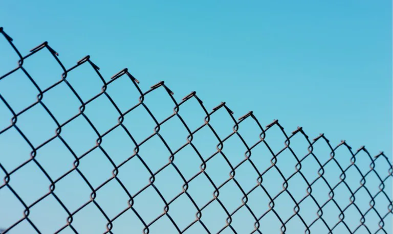 "Close-up of a chain-link fence against a clear blue sky."